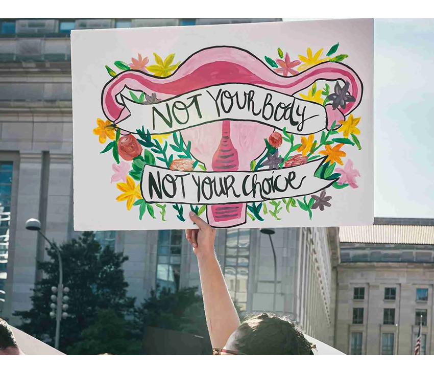 Person holding up a sign that says "Not your body, not your choice"